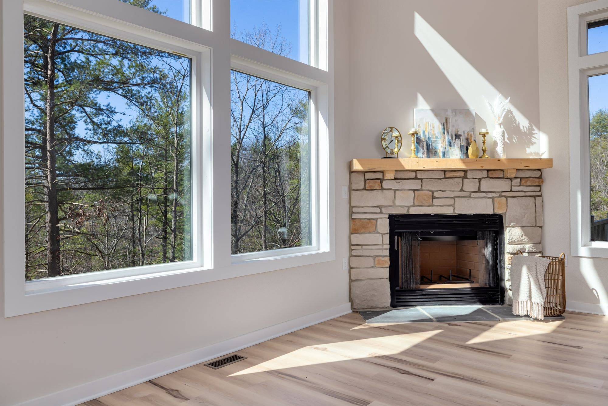 Stone fireplace beside tall windows onto the woods